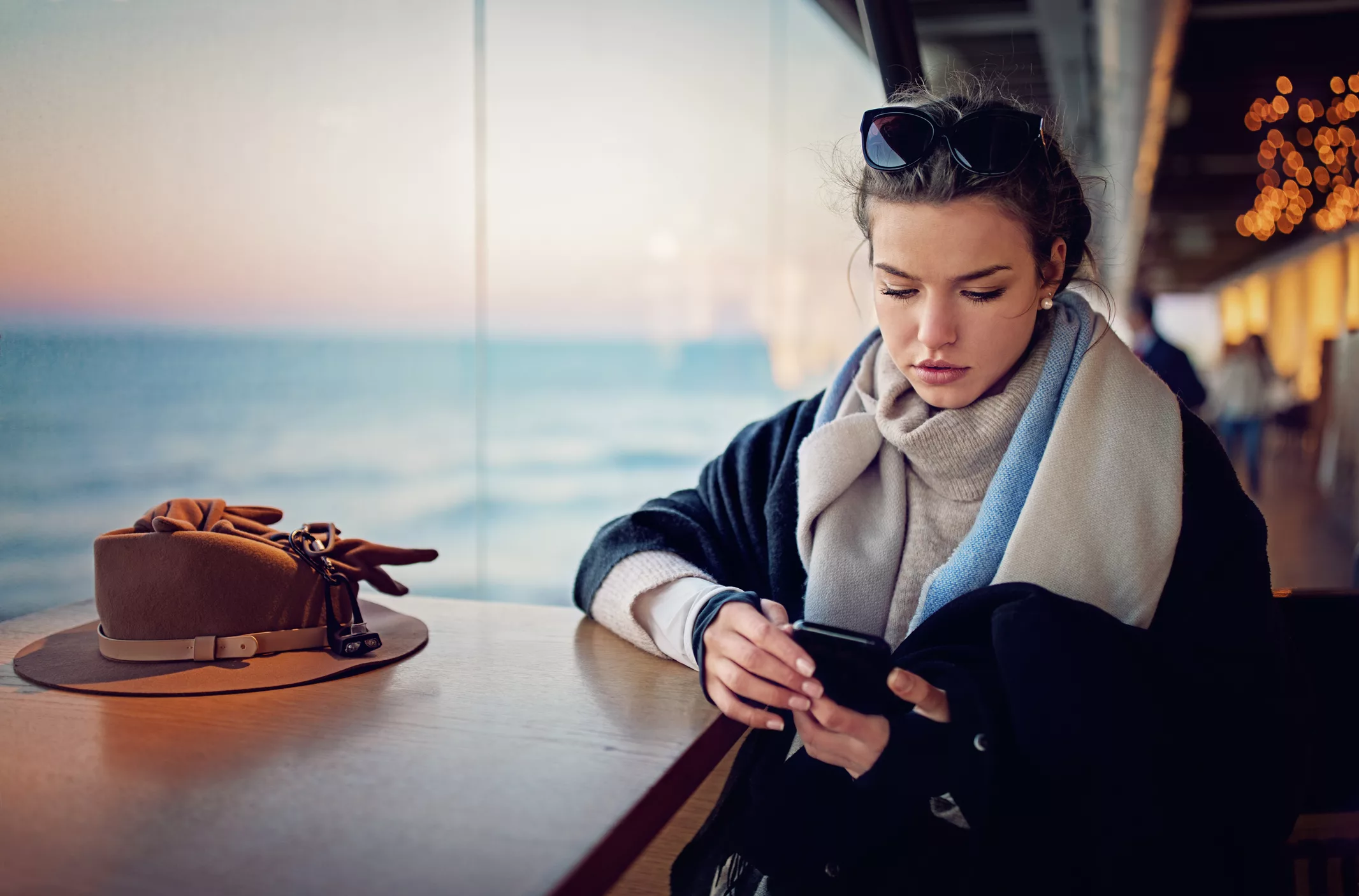 A young lady using her smartphone, sat next to her hat and gloves on the deck of a Danube River cruise ship