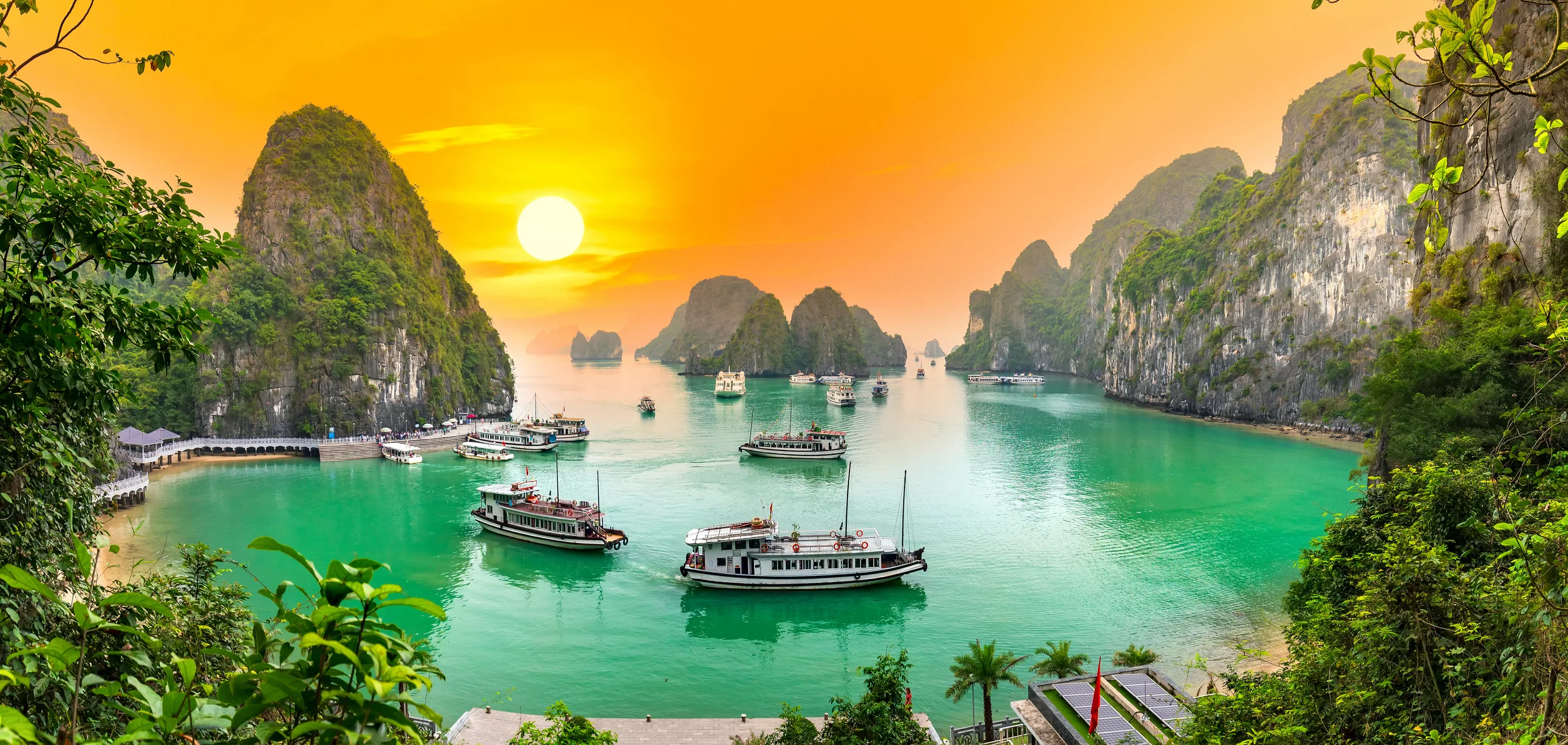 Hạ Long Bay at sunset, with emerald waters and a number of boats anchored in the bay.